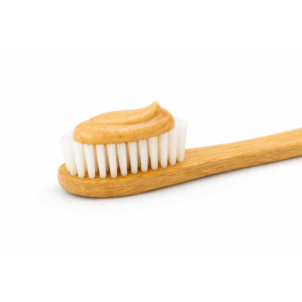 Bamboo dog toothbrush with peanut butter flavored dog toothpaste on the bristles, isolated on a white background.