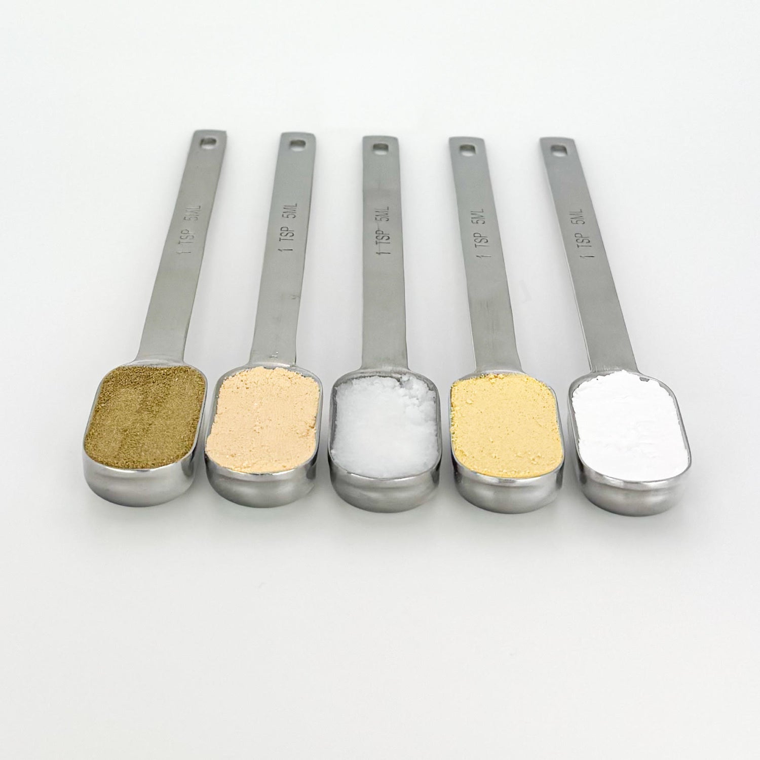 Organic dog toothpaste ingredients measured in spoons, including peanut butter and pumpkin powders